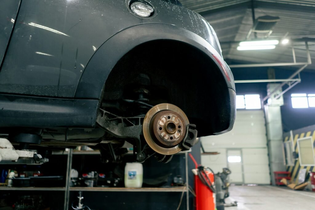 At the service station there is a gray car in a suspended state without a wheel a rusty part